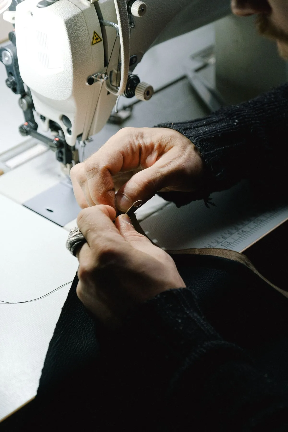 Hands sewing fabric beside a sewing machine; illustrative workshop photograph